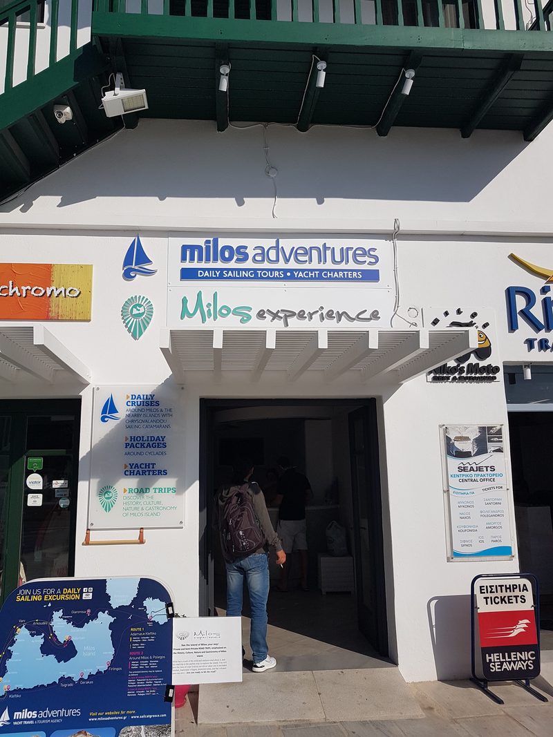 Harbourside rental agency signage in Adamas including a motorbike hire board next to the ferry ticket offices