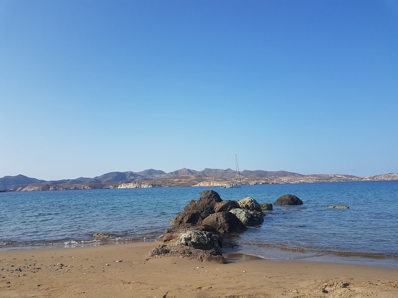 A quiet sandy beach near Pollonia, calm water and a sailboat anchored offshore